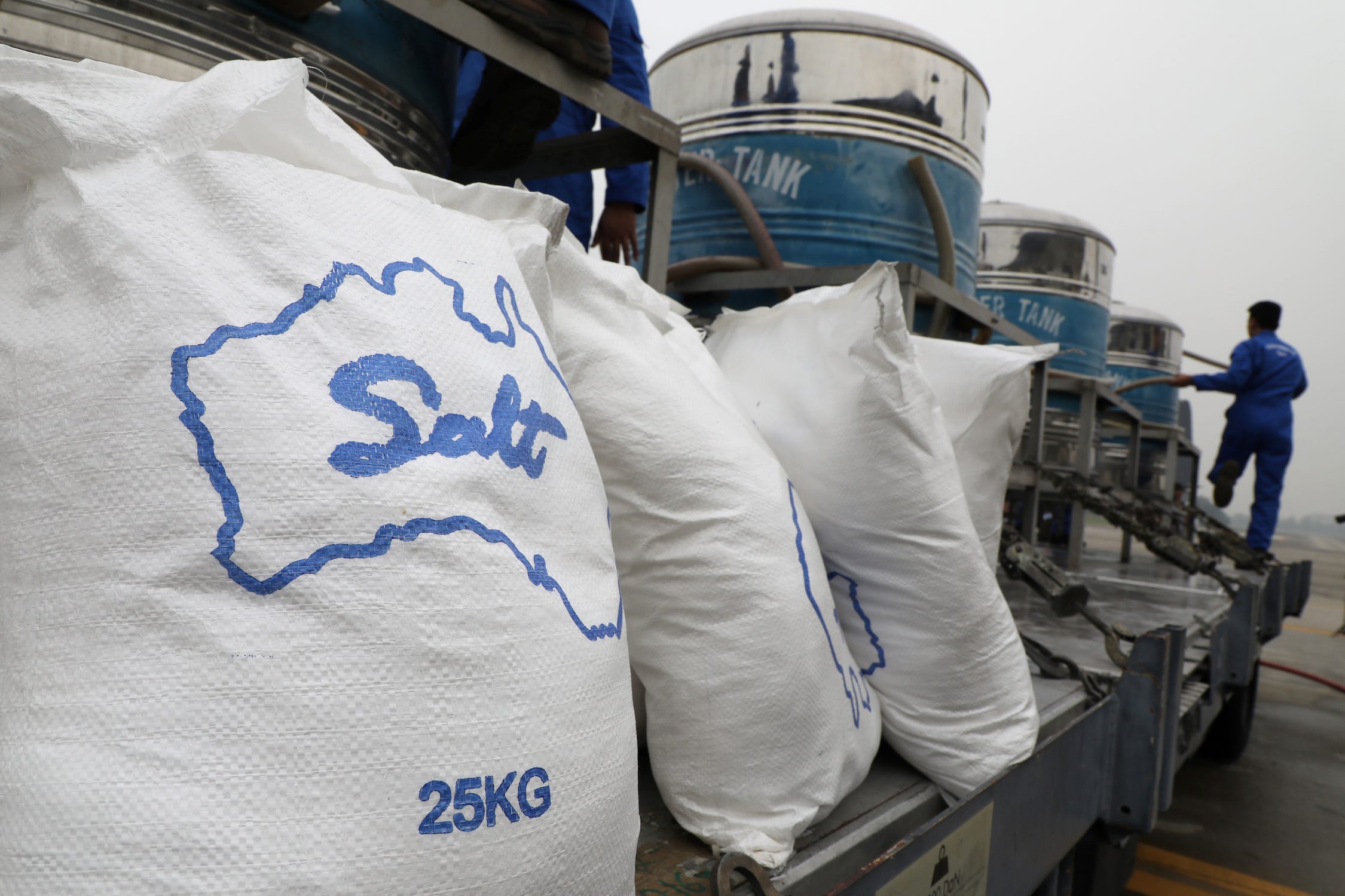 Weiße Säcke mit der Aufschrift „Salz 25 kg“ reihen sich auf einer langen LKW-Ladefläche aus Metall auf, auf der blaue und silberne Tanks stehen