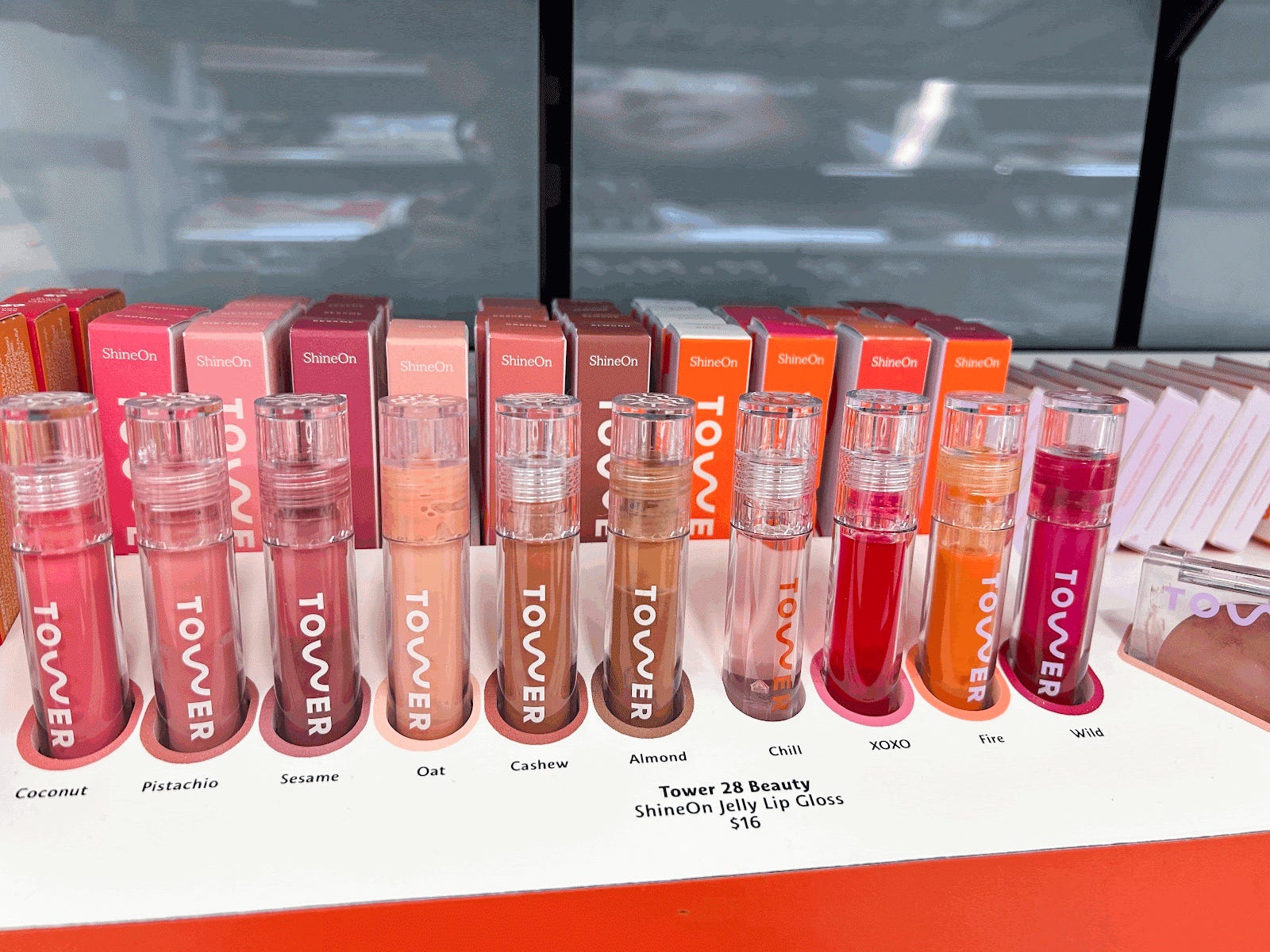 Mehrere rosa, hellbraune und orangefarbene Tower 28-Lipglosse auf einer Ausstellung bei Sephora