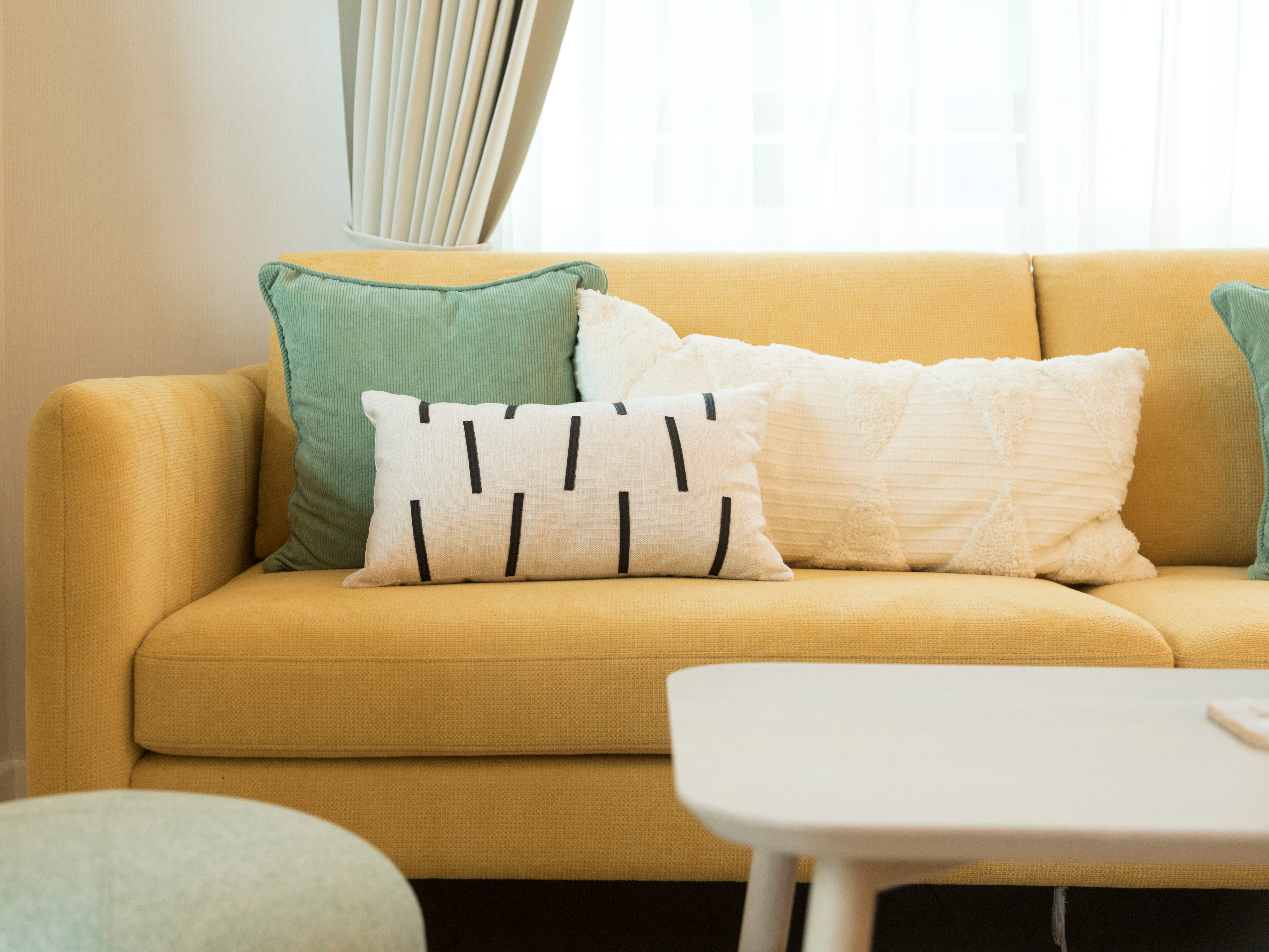 Eine große gelbe Couch mit weißen und grünen Kissen füllt das Wohnzimmer