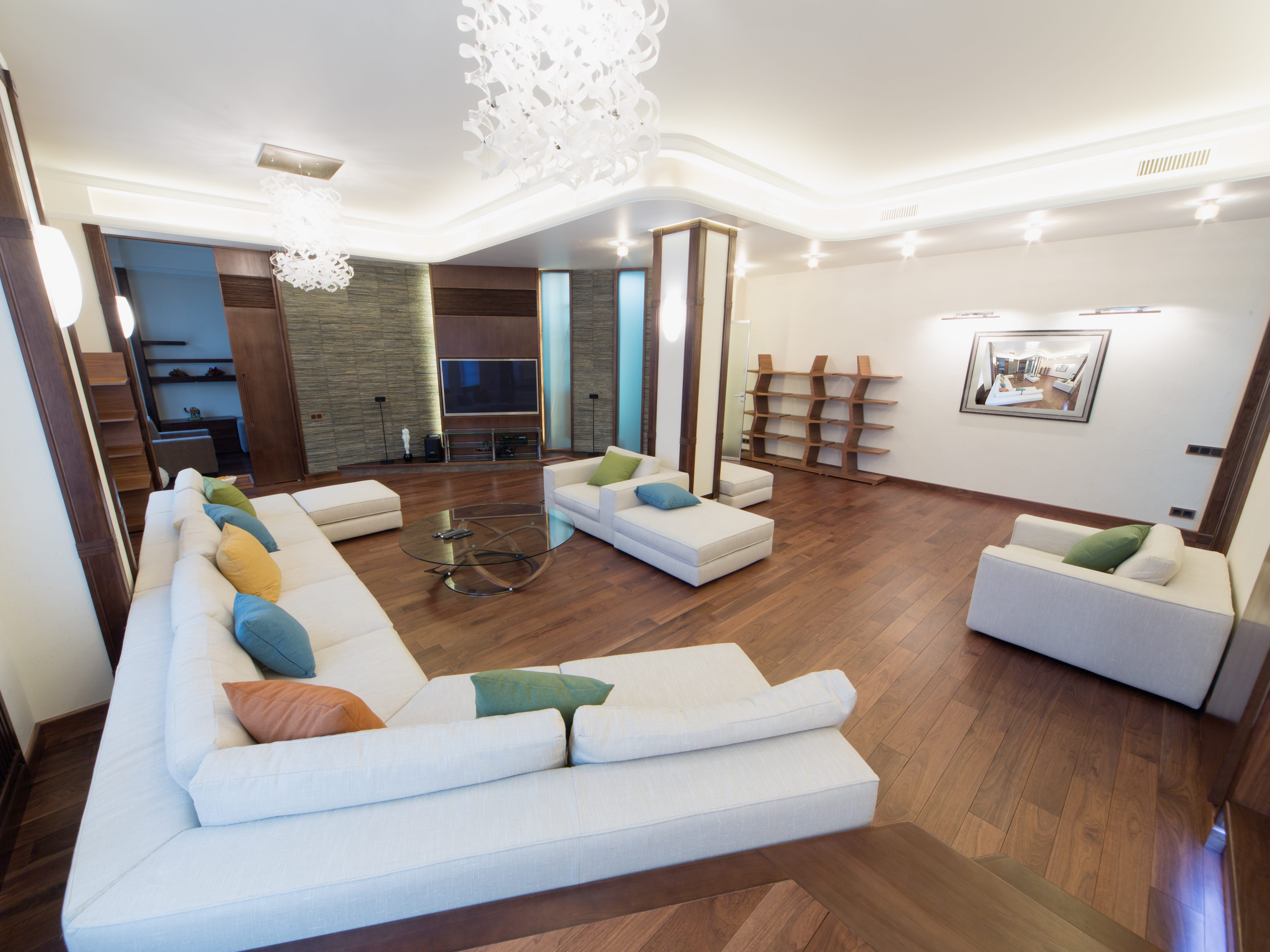 Wohnzimmer mit Holzboden, weißem Sofa und Stühlen, einem Kronleuchter und mehreren Lichtern an der Wand