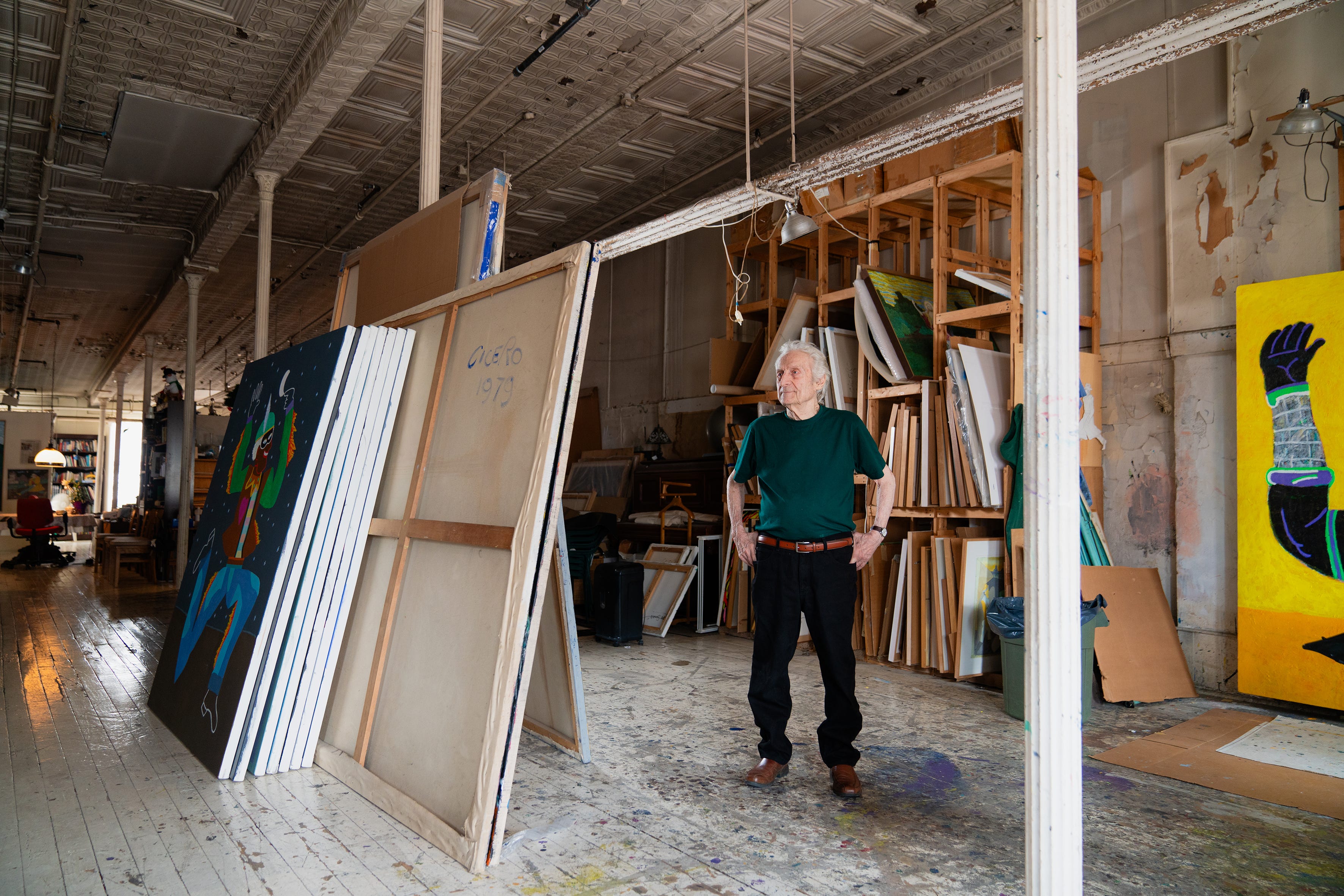 Carmen Cicero steht zwischen riesigen Gemälden, die in seinem rohen Industrie-Loft an einer Stange aufgestapelt sind.