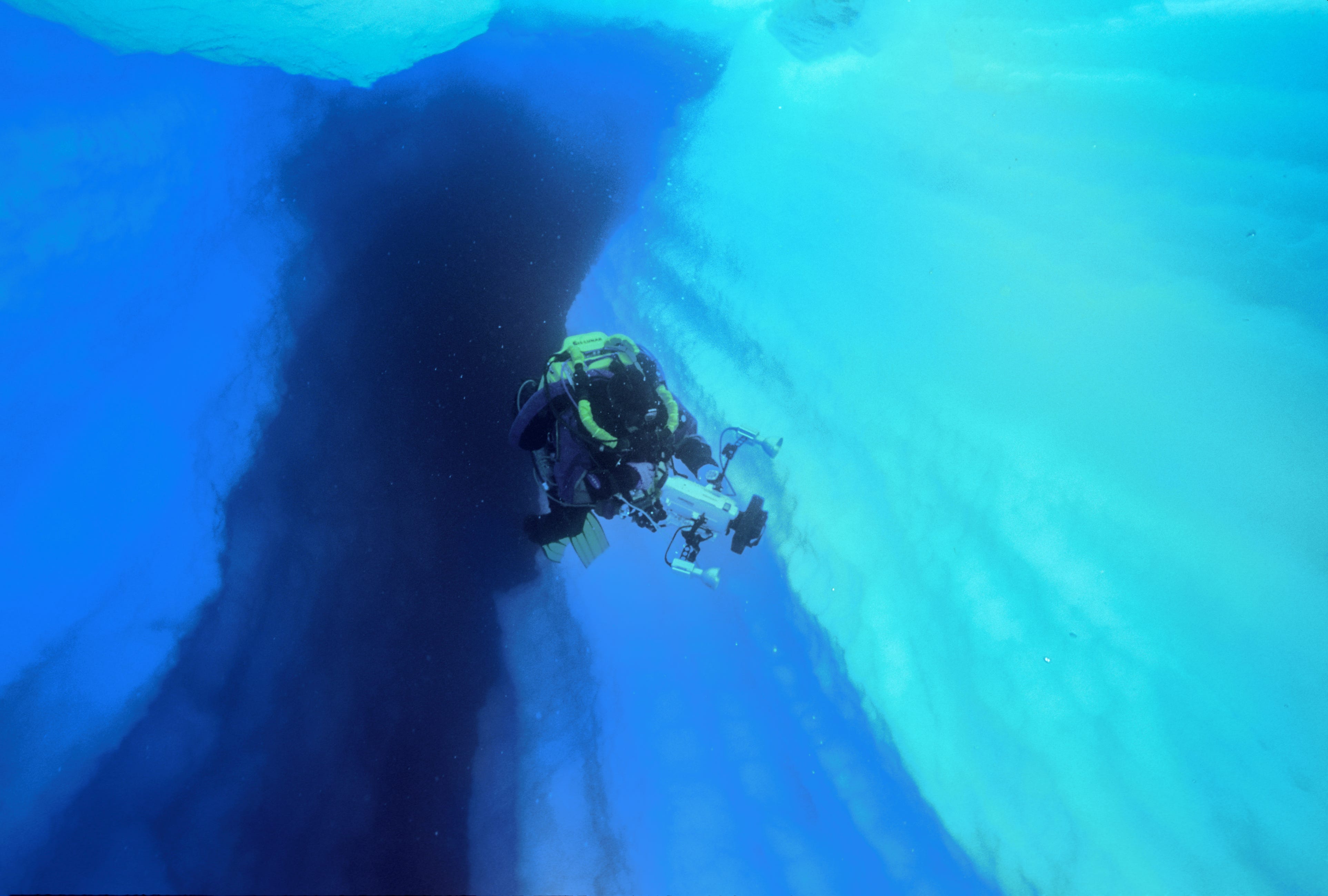 Ein Taucher schwimmt mit einer Kamera durch eine Gletscherspalte im Eisberg B15