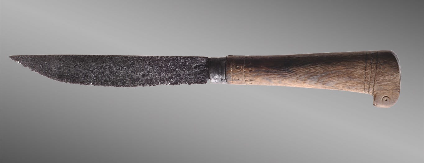 Knorriges Eisenmesser mit graviertem Holzgriff vor grauem Hintergrund