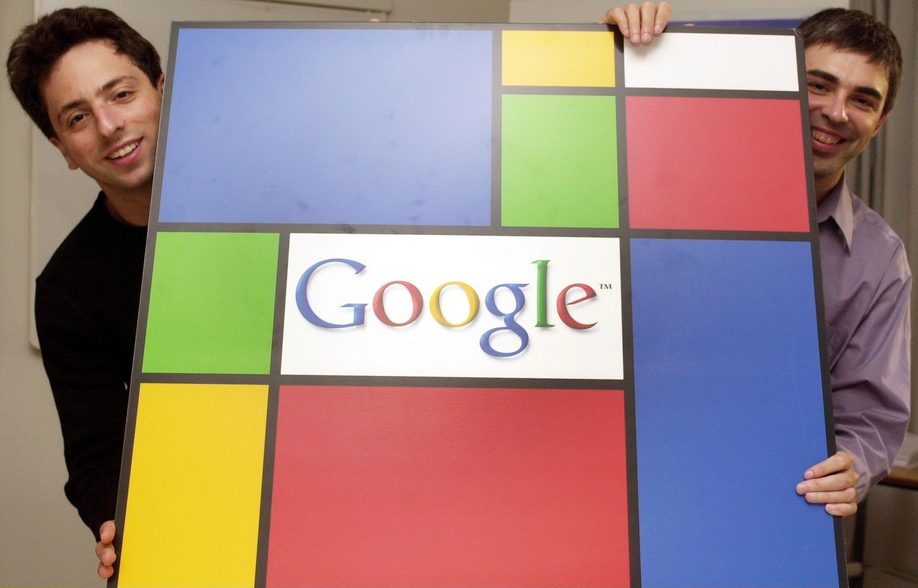 Sergey Brin und Larry Page posieren im September 2003 mit einem Google-Logo im abstrakten Stil von Piet Mondrian, das von beiden Seiten des großen Displays hervorlugt.
