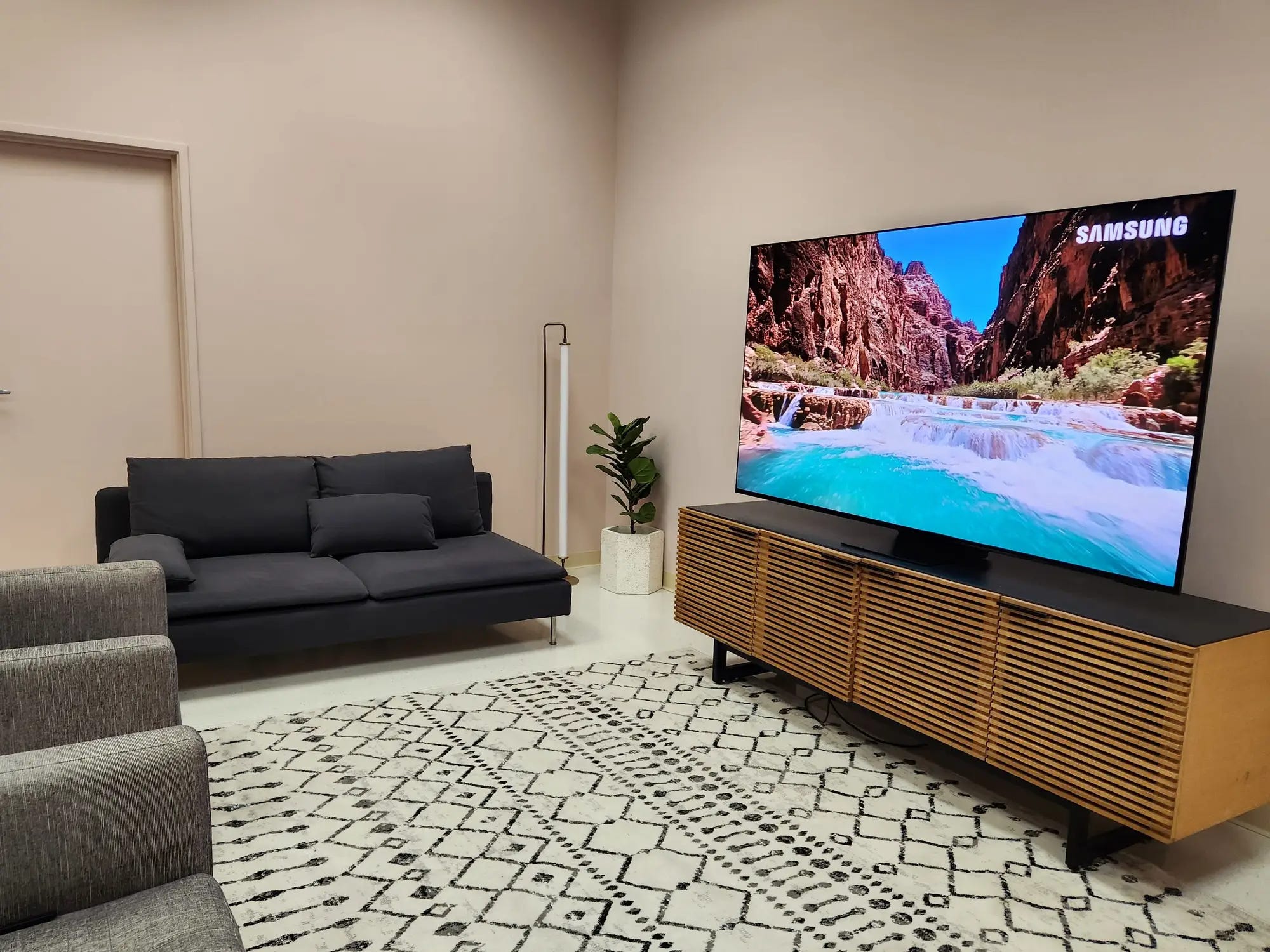 Ein Samsung S95C 4K-Fernseher steht auf einem Fernsehständer im Wohnzimmer und zeigt eine Szene mit einem Fluss und Bergen.