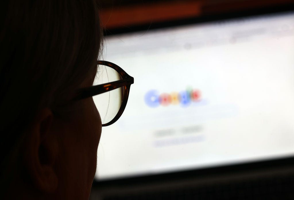 Eine schattenhafte Person mit Brille sitzt vor einem verschwommenen Laptop-Bildschirm, auf dem die Google-Suchmaschine angezeigt wird.