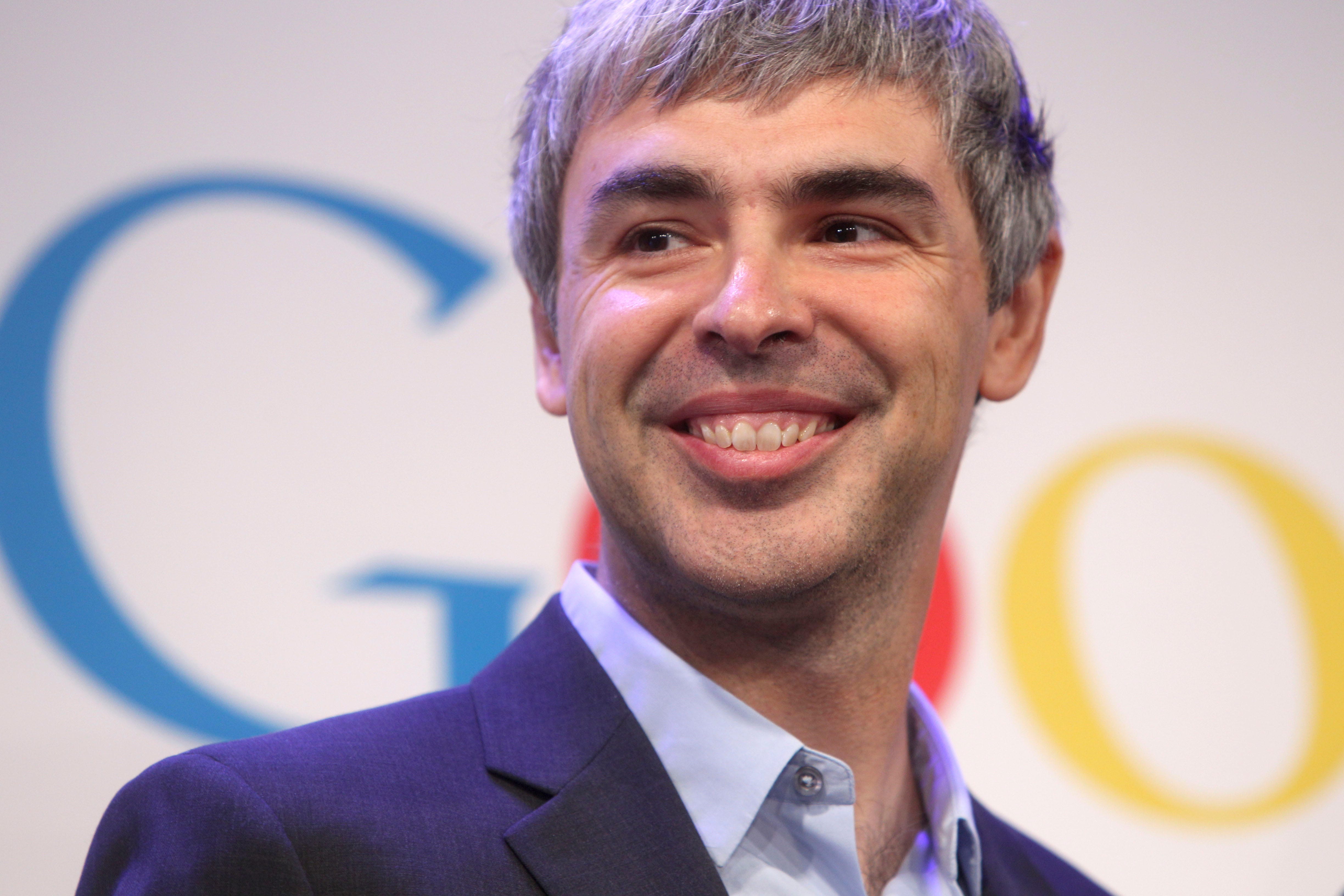 Der ehemalige Google-Chef Larry Page lächelt vor dem Google-Logo.