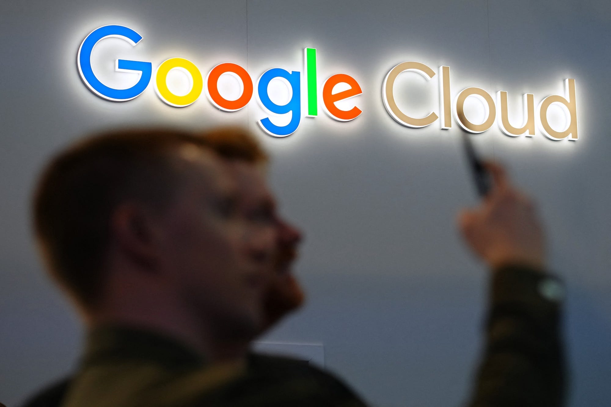 Zwei verschwommene Figuren mit einem Smartphone stehen vor dem Google Cloud-Logo an einer Wand.