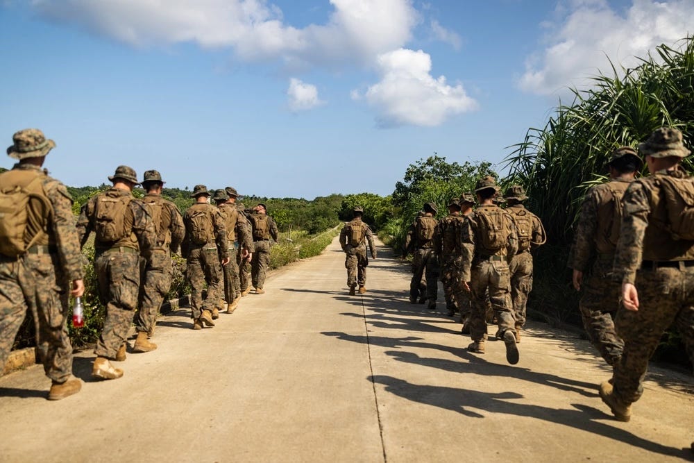 Eine Reihe US-Marines gehen eine von Bäumen gesäumte Straße entlang