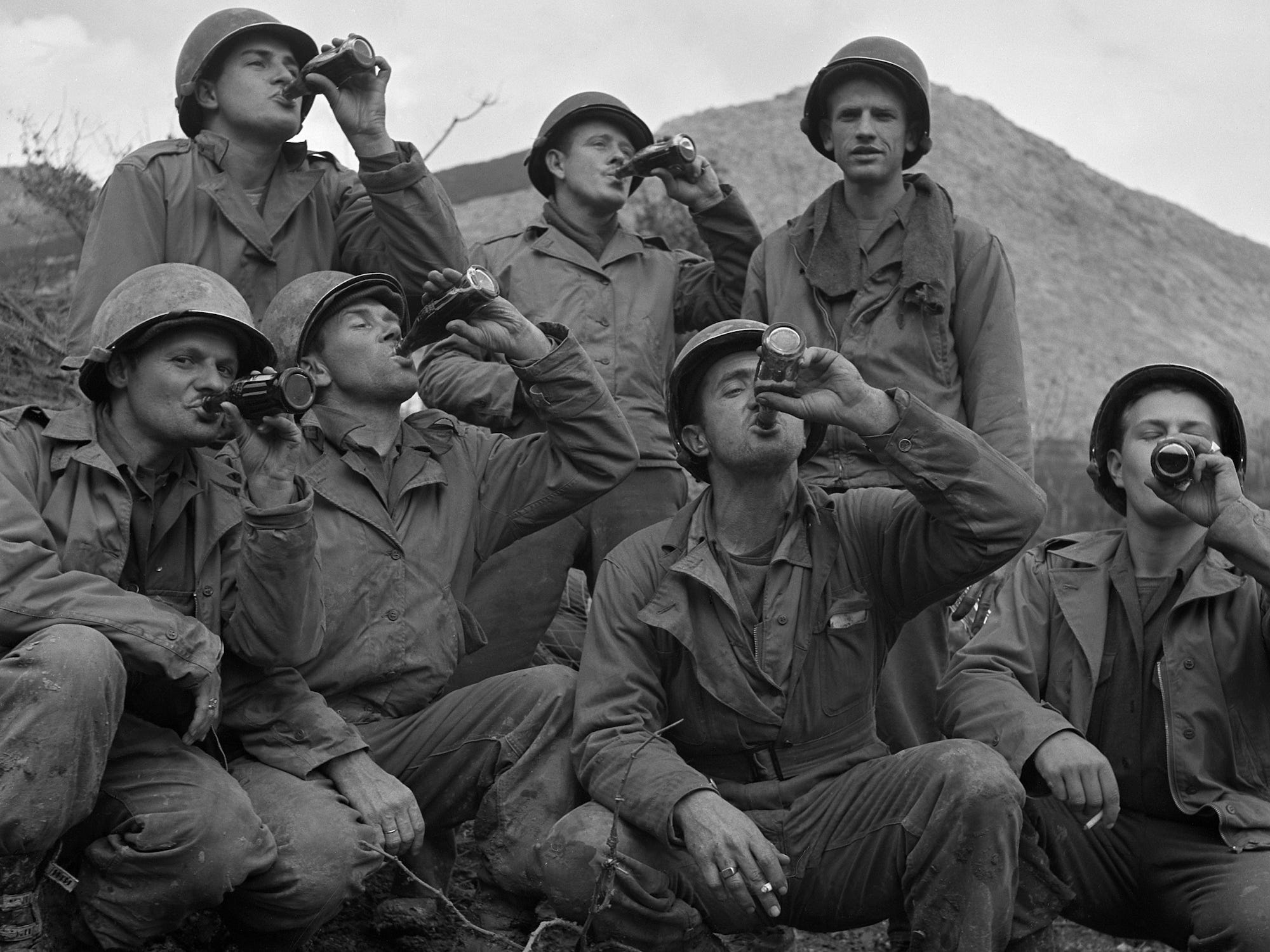 Eine Gruppe US-Soldaten mit Helmen und Arbeitsanzügen trinkt Coca Cola in Italien