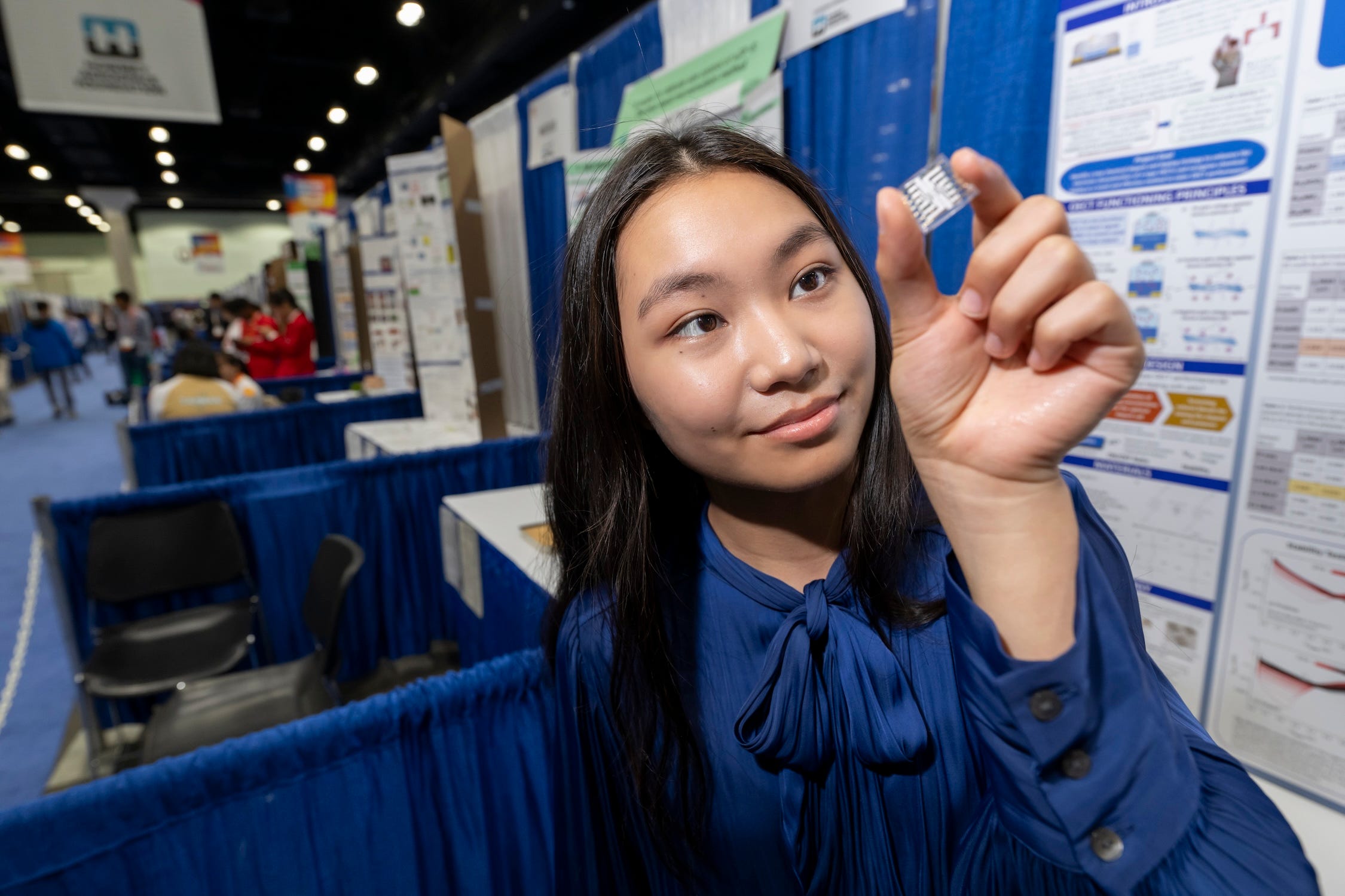 Ein Mädchen in blauem Hemd und langen dunklen Haaren hält ein kleines OETC-Gerät in der Hand, das wie ein kleines klares Quadrat mit weißer Innenseite aussieht