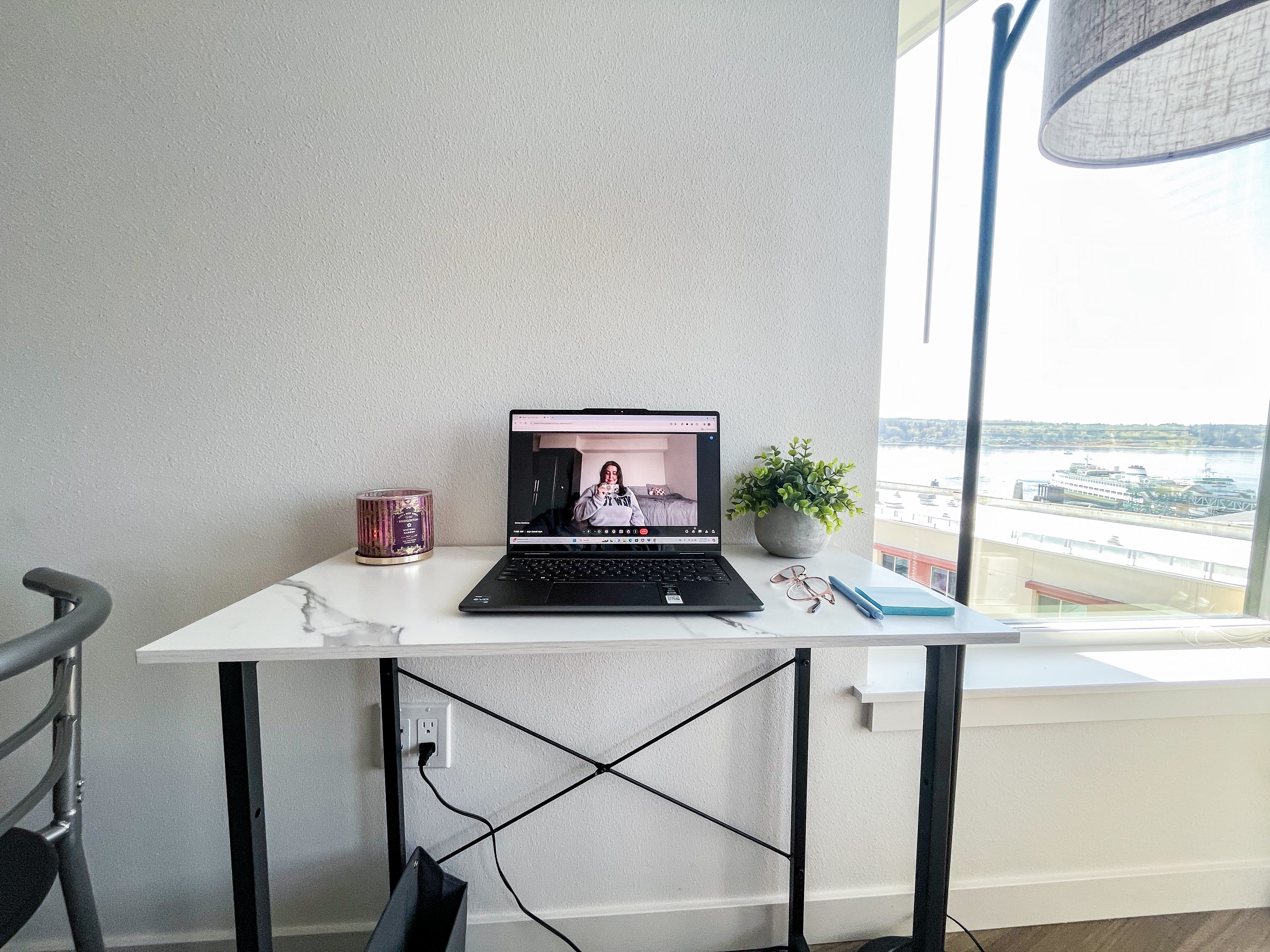 Vorderansicht eines weißen Schreibtisches mit einem Laptop-Bildschirm und einer Kamera, auf der der Autor zu sehen ist.  Der Tisch steht neben einer Lampe und einem Fenster