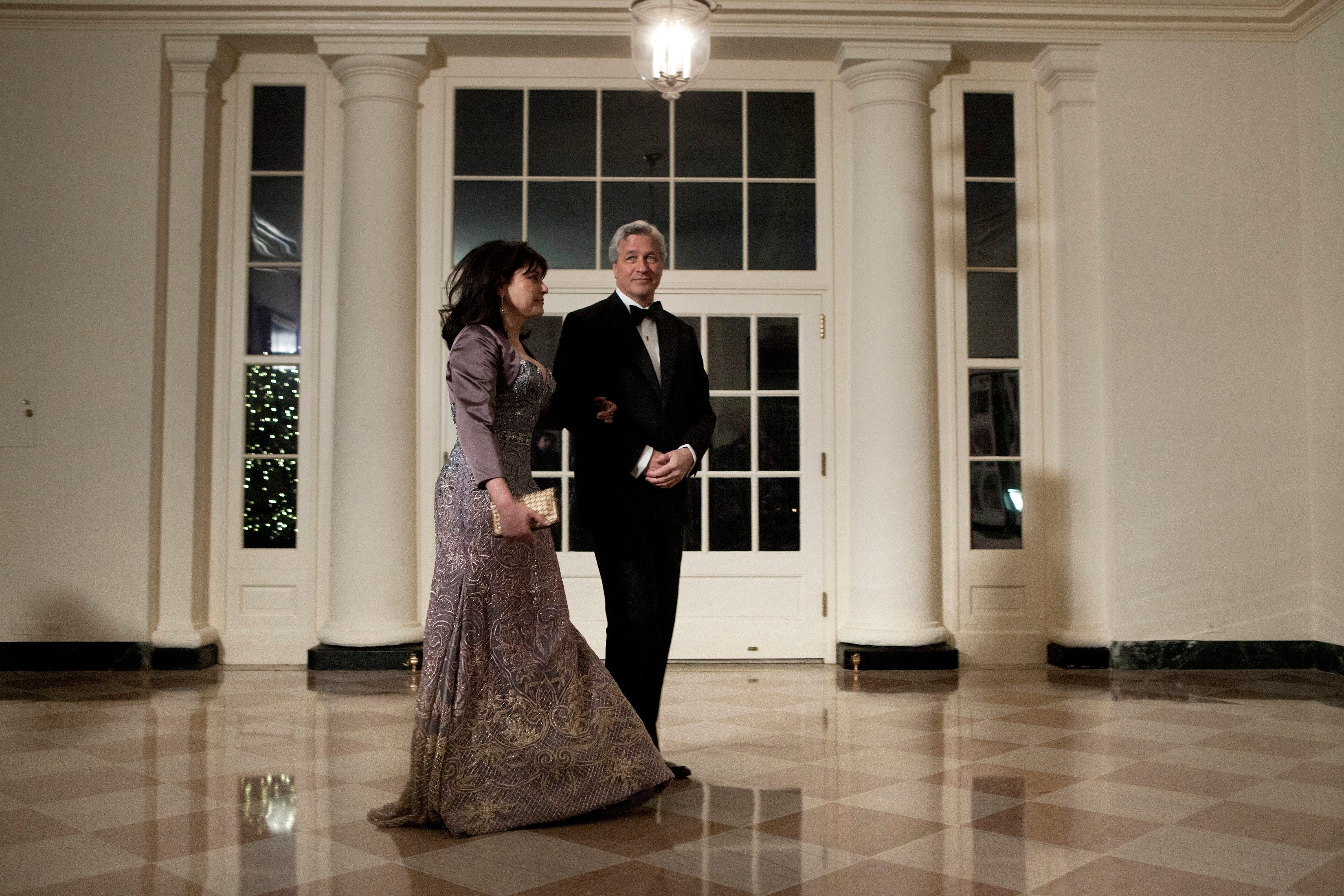 Jamie Dimon und seine Frau Judith gehen in schwarzer Abendgarderobe über den Marmorboden des Weißen Hauses.