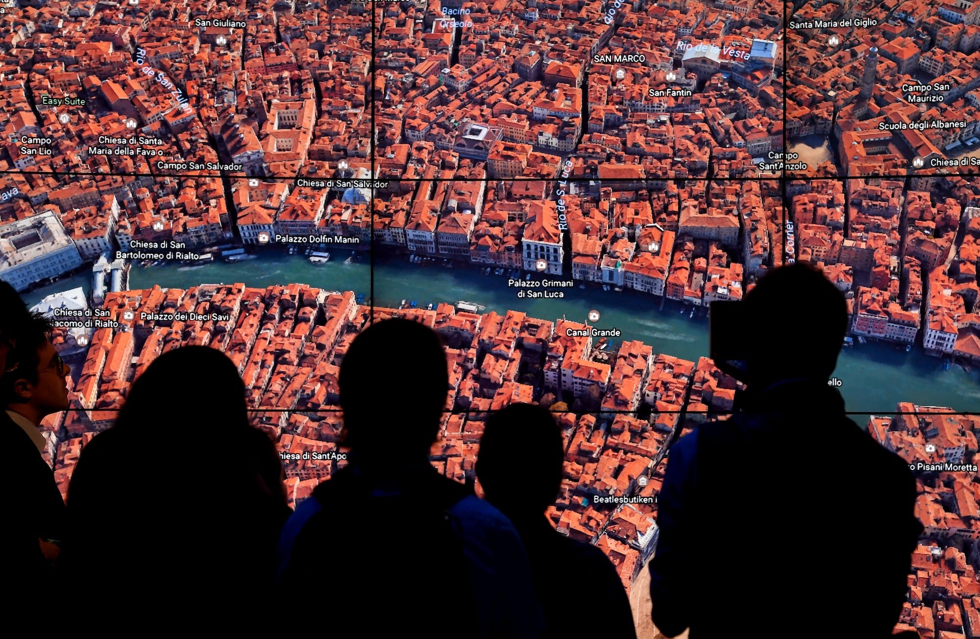 Eine Gruppe von Menschen steht vor einem großen Bildschirm, auf dem ein Satellitenbild von Italien von Google Earth zu sehen ist.