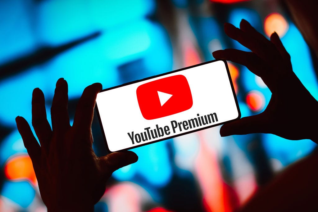 Zwei schattenhafte Hände halten ein Smartphone hoch, auf dem das YouTube Premium-Logo angezeigt wird.