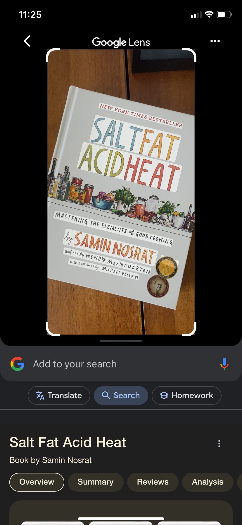 Ein Screenshot von Google Lens zeigt das Bild eines Buches auf einem Tisch. In den Suchergebnissen wird der Titel „Salt Fat Acid Heat“ von Samin Nosrat aufgeführt.