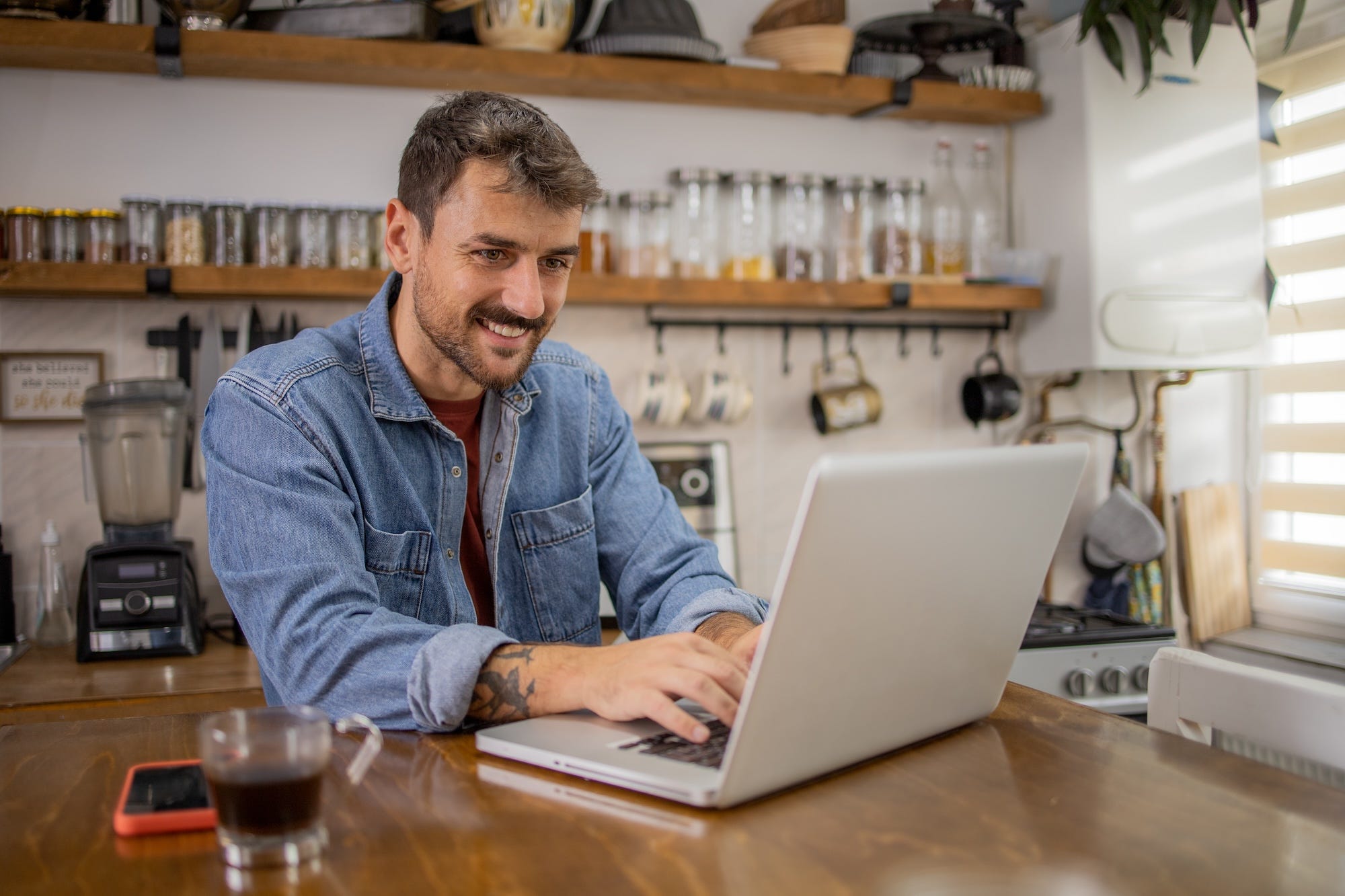 Ein Geschäftsinhaber in einem Café lächelt, während er auf seinem Laptop tippt.