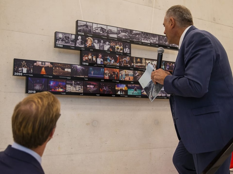 Two men look at small pictures installed in the entrance to the reopened hall.