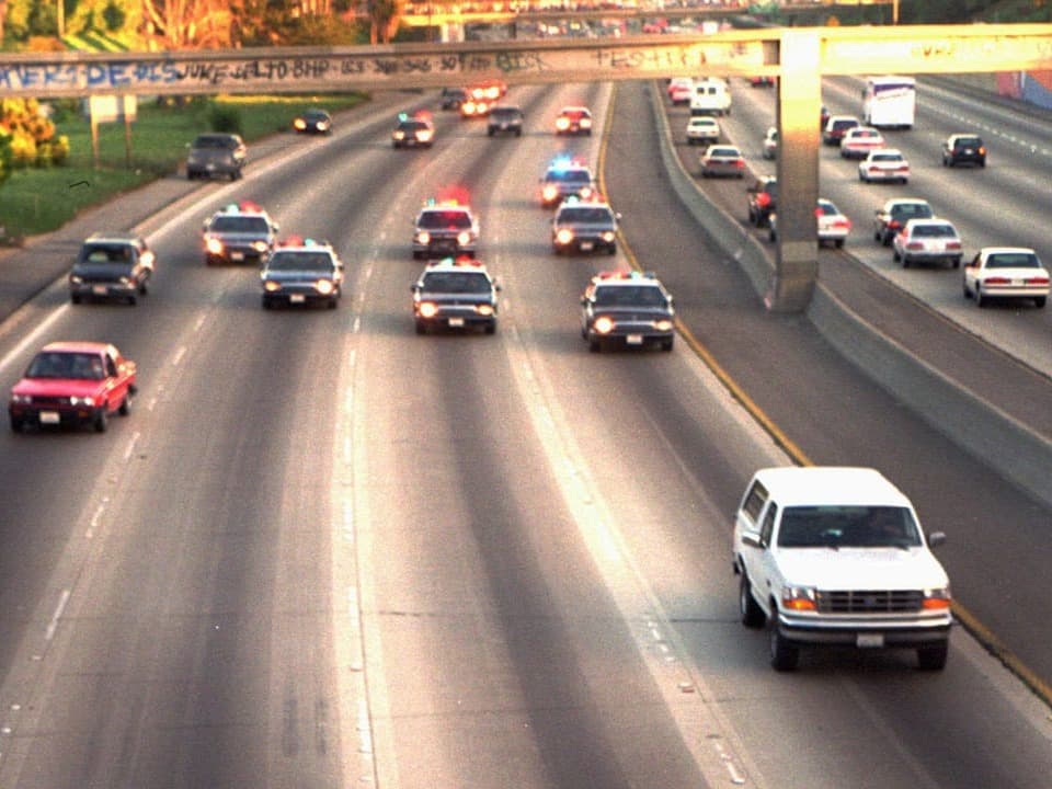 A white car is being chased by police cars on the highway.