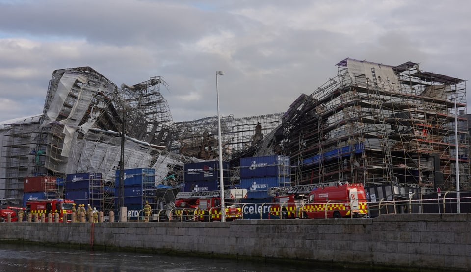 Collapsed building with scaffolding and fire trucks in front of it