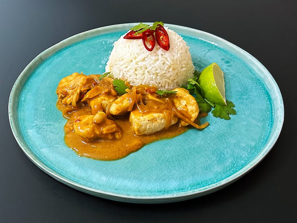 Plate with curry chicken, rice, lime wedge and chili on blue plate