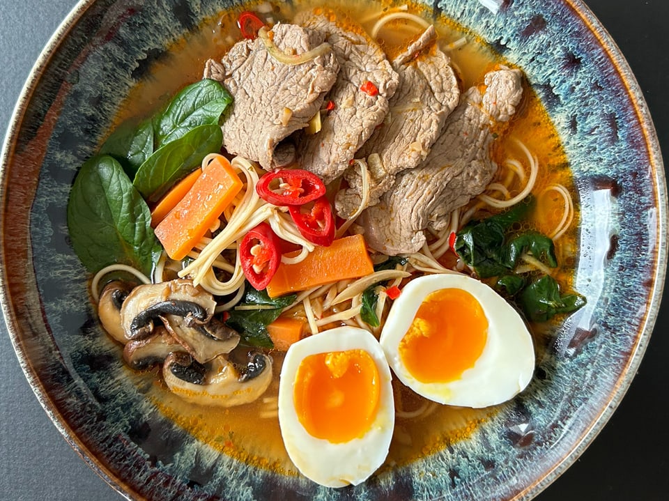 Asian noodle soup with beef, vegetables, mushrooms and halved eggs on a colorful plate.