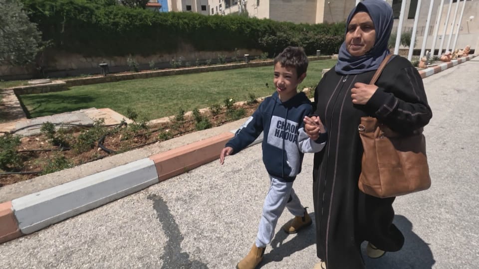 Awatef holds her son Naeem's hand.  They walk together on a sidewalk to the hospital. 