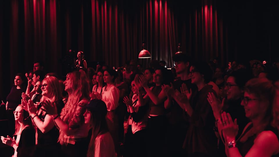 Crowd clapping at a concert in red stage lights.