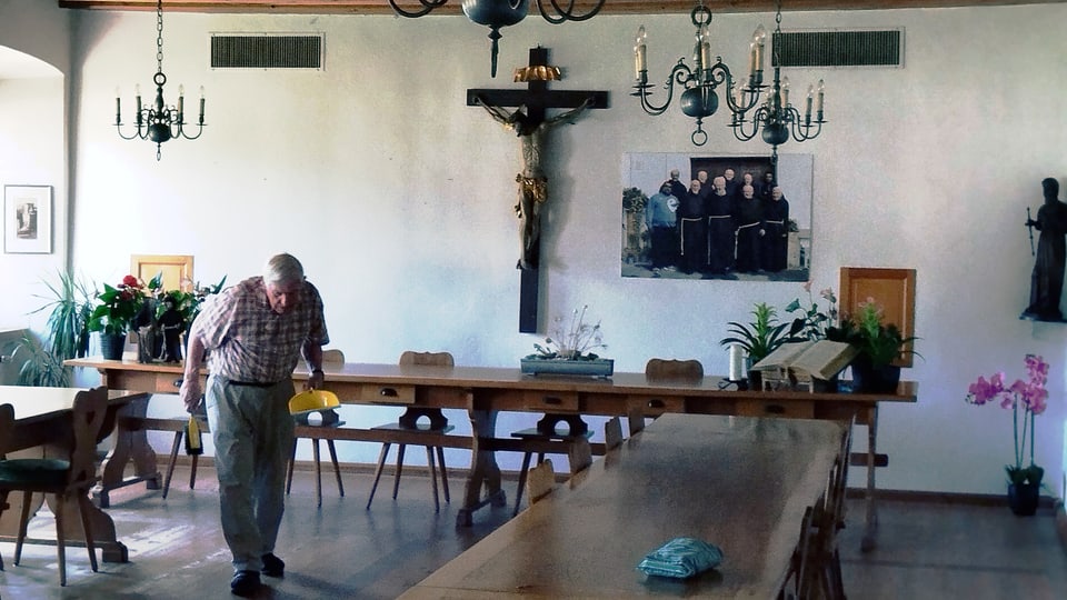 Elderly man walks through a room with long tables and chandeliers