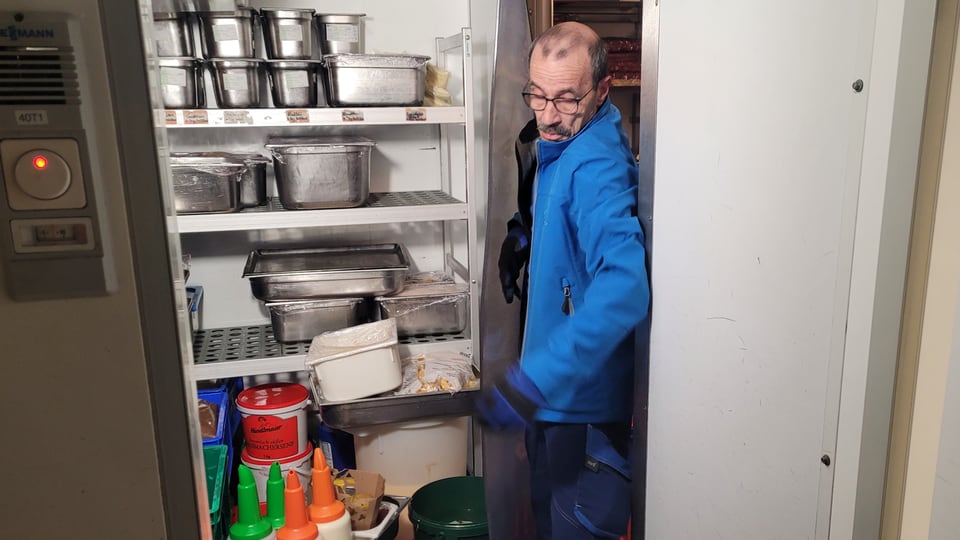 A man squeezes through a narrow entrance into a cluttered food warehouse.