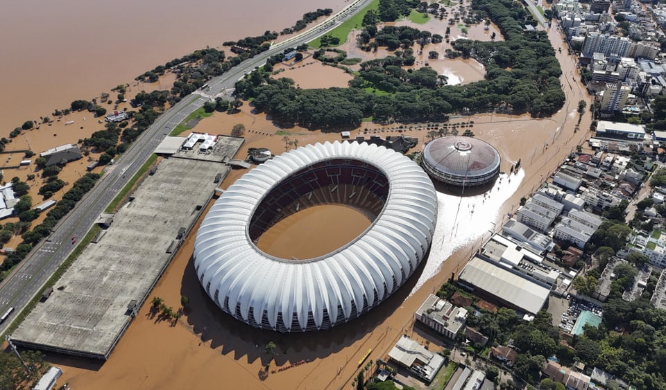 Aerial view of an oval-shaped stadium and its surroundings.  Floodwaters have flooded the streets and interior areas.