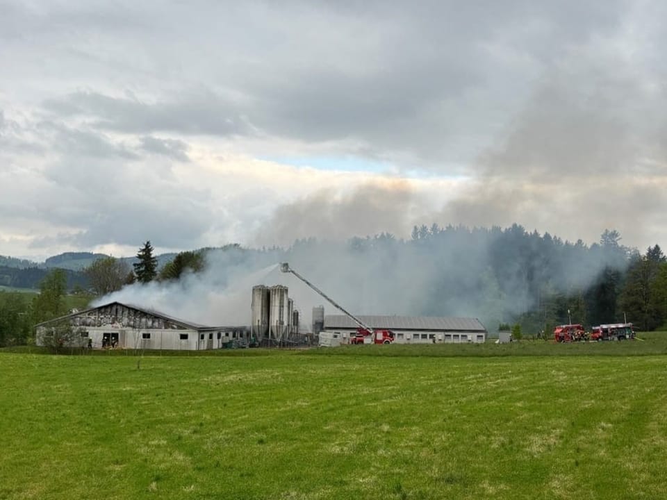 Burning barn with firefighters in a rural area.
