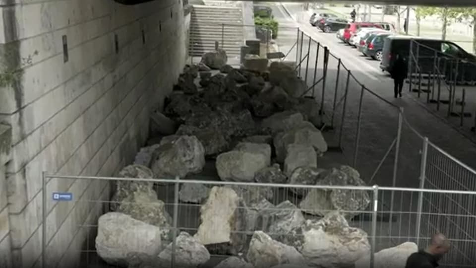 Construction work in progress with a barrier and a pile of large stones on an urban sidewalk.
