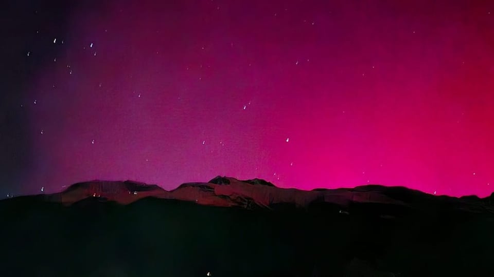 Mountain silhouette with pink northern lights and starry sky.