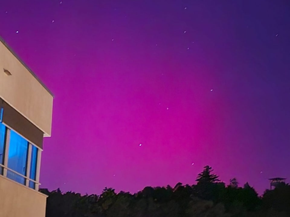Corner of building with illuminated window against a night sky in pink and purple