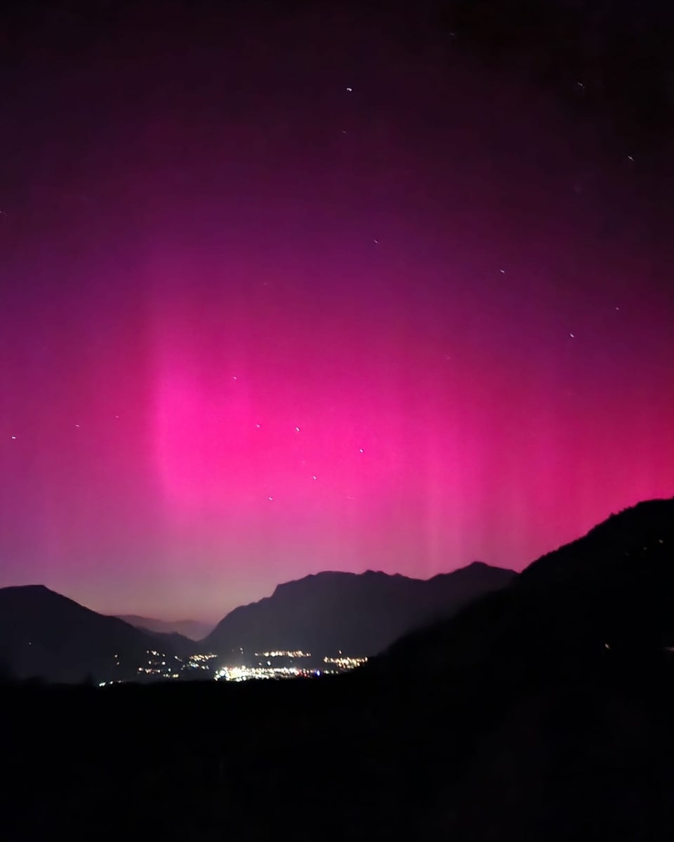 Northern lights in pink and purple over mountainous landscape at night.