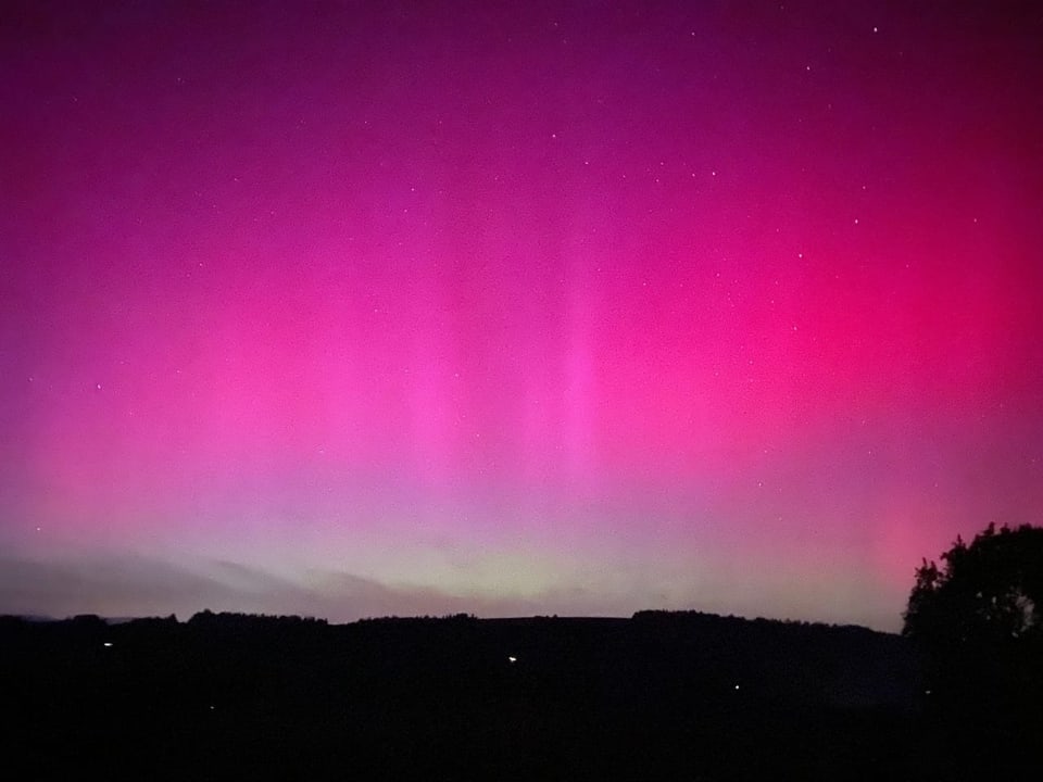 Northern lights in pink and purple over a hilly landscape at night.