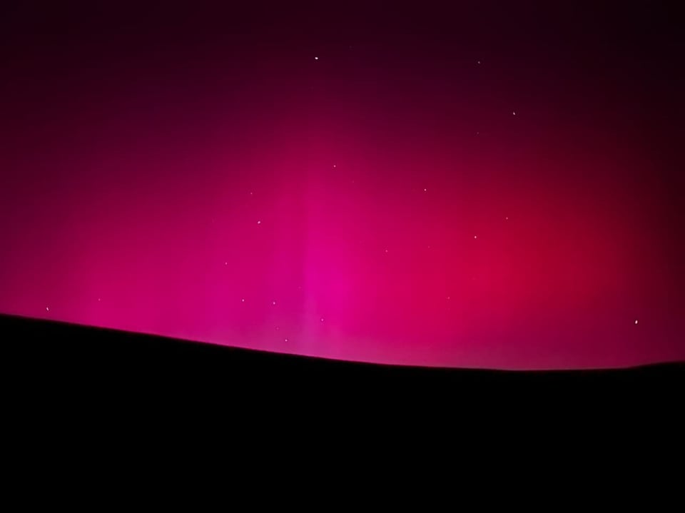 Red northern lights over a dark hilly landscape under a starry sky.