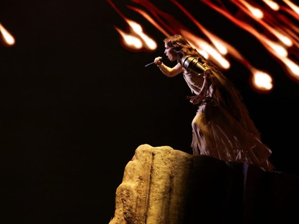 Sängerin in historischem Kostüm tritt auf einer Felsformation auf, mit dynamischen Lichteffekten im Hintergrund.