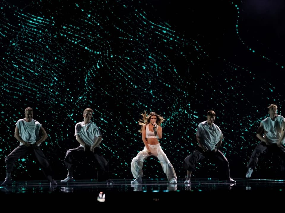 Sängerin und Tänzer auf einer Bühne mit grün-schillernder Lichtshow im Hintergrund.