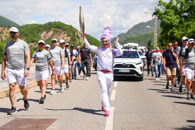 This photo taken and released on May 11, 2024 by the Organizing Committee for the Paris 2024 Olympic and Paralympic Games (Cojop) shows French drag queen Miss Martini holding the Olympic flame as part of the torch relay, in the streets of Digne-les-Bains.