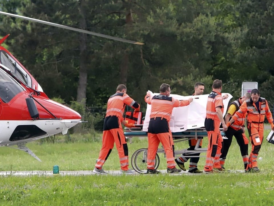 Rescue workers transport a person on a stretcher, accompanied by security forces and media representatives.