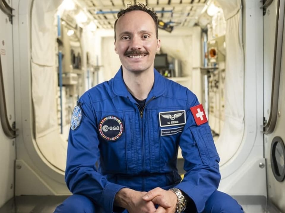 Astronaut in blue uniform sits in a spaceship module.