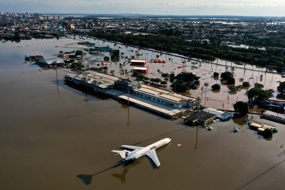View of an airport building with an airplane in front of it.  Both are surrounded by brown floodwaters.  Everything is flooded