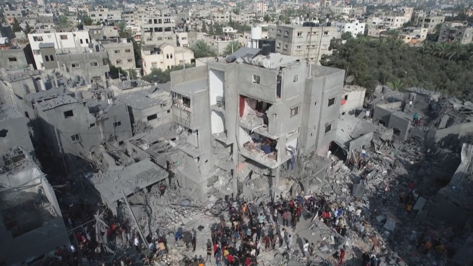 A picture of a destroyed apartment block.  People are standing in front of the building.