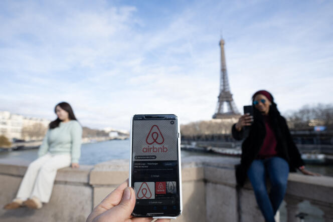 A woman holds her cell phone with the Airbnb application while others pose in front of the Eiffel Tower, in Paris on February 2, 2024.